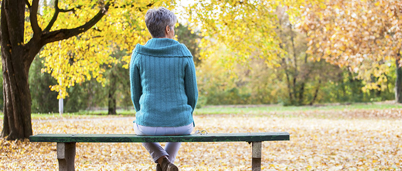older woman sitting on a bench looking at changing leaves on trees