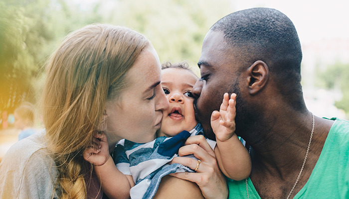 A mother and father are kissing their baby