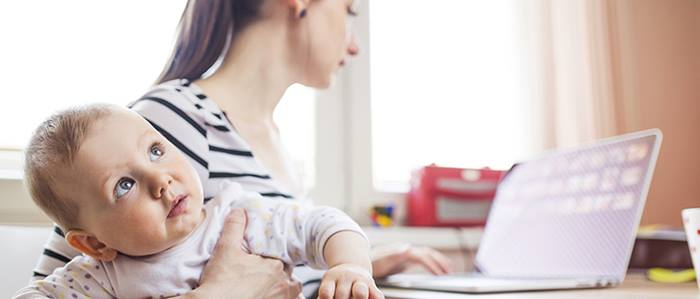 A mother is using the computer while taking care of her baby