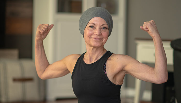 Post-treatment exercise helps with cancer recovery Female cancer survivor flexes muscles