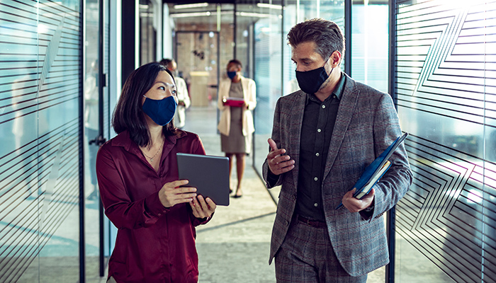 Colleagues discuss work while walking down office hallway