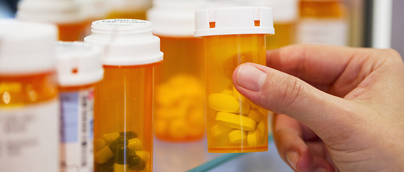 hand taking a bottle of pills out of a medicine cabinet