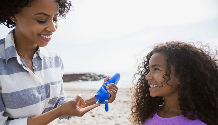 Mother applies SPF to daughter at beach