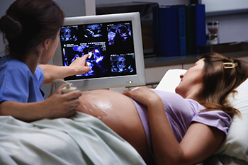 A pregnant patient looks at a live ultrasound of her baby with a technician.