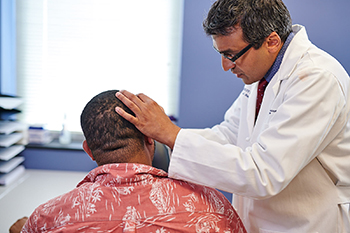 Dhruv Singhal, MD, examines a patient's head and face for lesions.