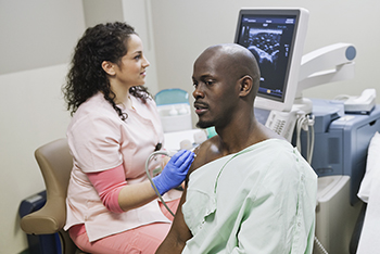 An x-ray technician performs and ultrasound exam on a patient's shoulder.