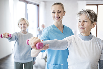 A physical therapist helps a senior patient with her form in a weight class.