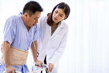 A doctor helps an elderly patient use an adult walker.