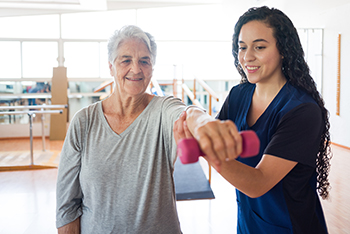 A physical therapist helps a senior citizen lift weights during a session.