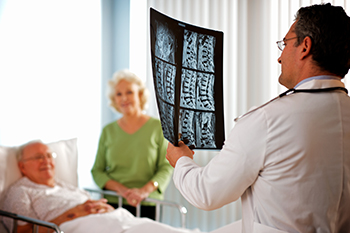 A doctor examines a patient's x-ray of the spine in front of the patient and his wife.